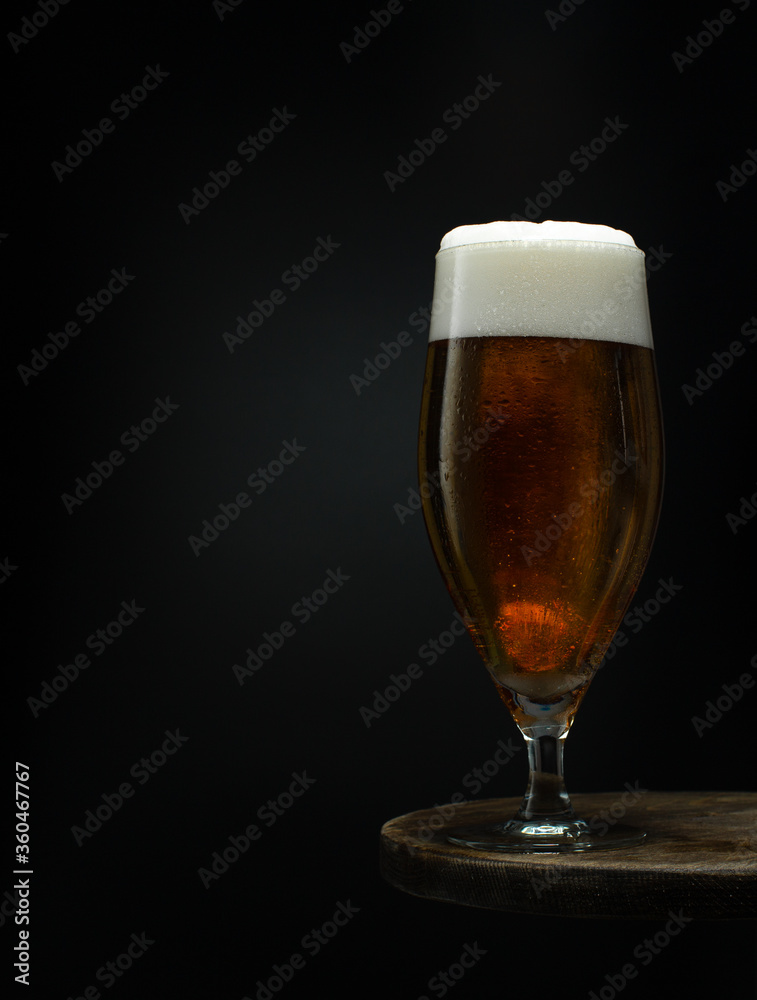 Glass of cold fresh beer with foam on wooden table on black background.Close up. Glass of cold fresh beer with foam on wooden table on black background.Close up.