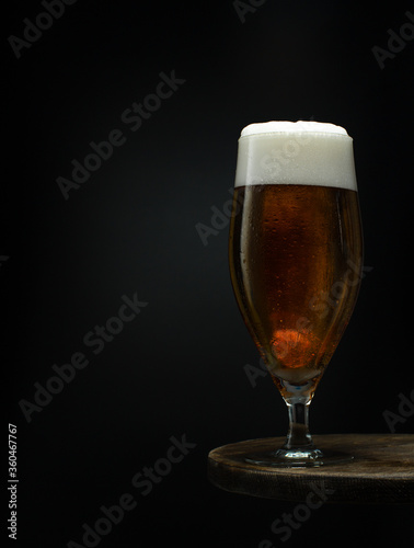 Glass of cold fresh beer with foam on wooden table on black background.Close up.