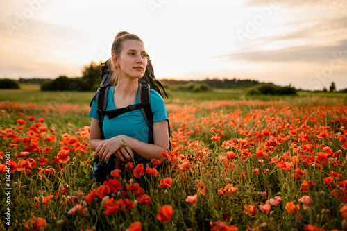 front view of young woman tourist who stands on field of red poppies.