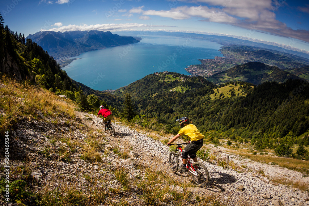 MONTREUX, SWITZERLAND. Two mountain bikers riding a narrow rocky trail above Montreux, Switzerland. Lake Geneva and the French Alps in the background.