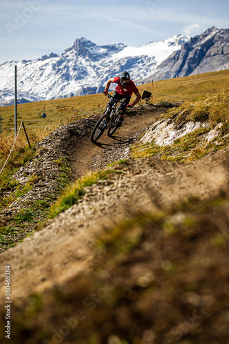 CRANS MONTANA, SWITZERLAND. A mountain biker riding a smooth 'Bermed' corner in the purpose built bike park. Snow capped mountains behind