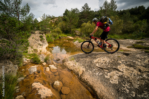 A mountain biker crossing a river carrying a large backpack. Huesca, Spain.