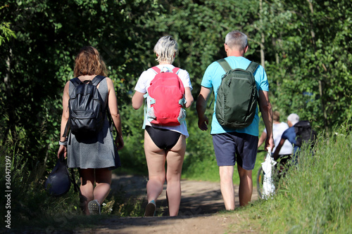 People with backpacks walking in a summer forest. Man and two woman travelling together, summer hiking and adventure