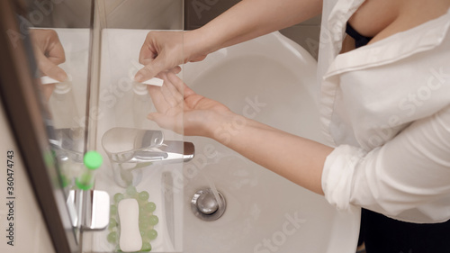 Sexy woman clicks on dispenser of soap bottle washing her hands after work. Hygiene and health concept.