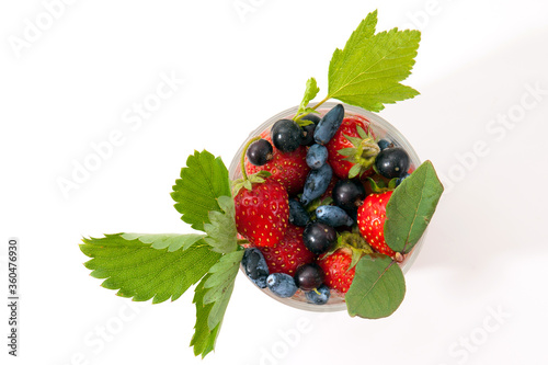 strawberries, currants, honeysuckle, berries in a glass with leaves on a white background top view photo