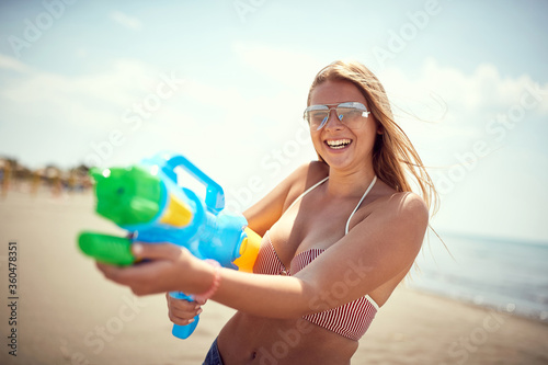 Sexy blonde girl on the beach with water gun.Crazy vacation with happy friends and  fun  at beach. photo