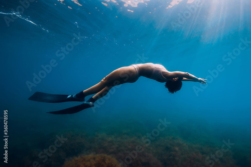 Fototapeta Naklejka Na Ścianę i Meble -  Sporty woman freediver with fins glides underwater in blue sea.