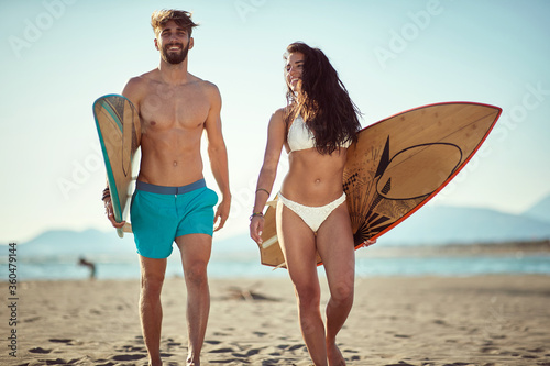 fit, sexy, young  male and female walking and talking on beach, holding surfboards, smiling