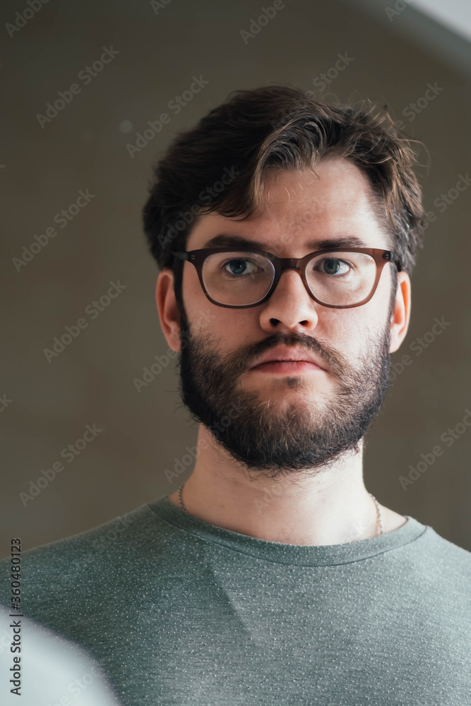 a handsome young man with a thick beard and glasses is illuminated on one side by a soft light. green t-shirt a handsome young man with a thick beard and glasses is illuminated on one side by a soft light. green t-shirt