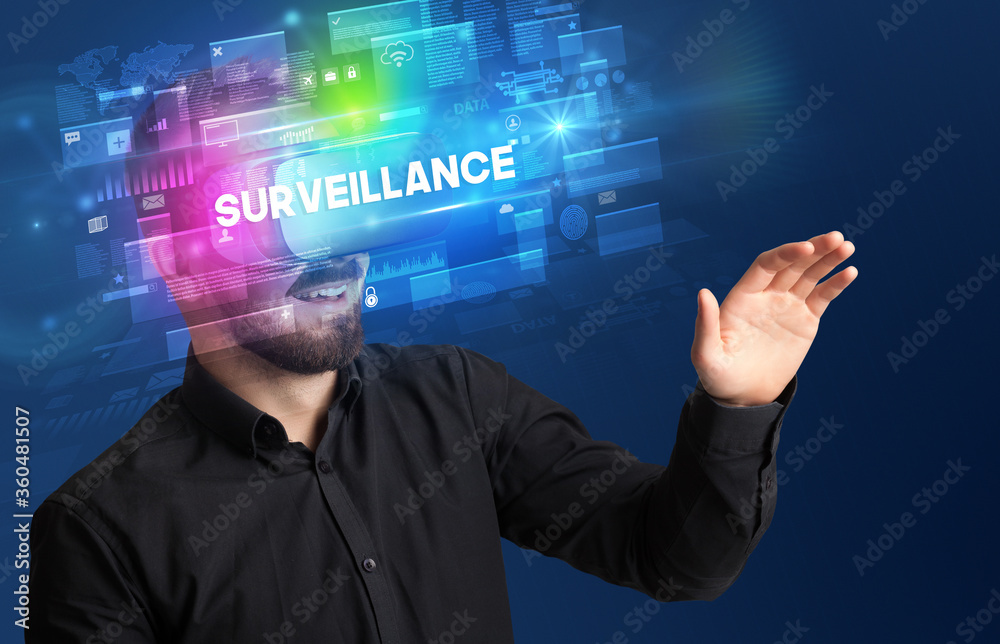 Businessman looking through Virtual Reality glasses with SURVEILLANCE inscription, innovative security concept Businessman looking through Virtual Reality glasses with SURVEILLANCE inscription, innovative security concept