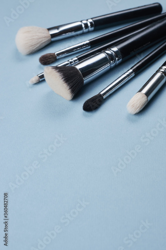 Fototapeta Naklejka Na Ścianę i Meble -  black brushes for makeup of different sizes and colors on a blue background. copyspace for text.