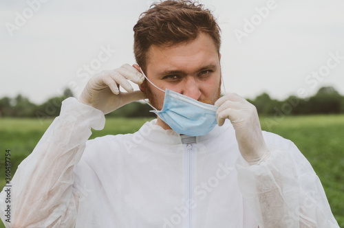 A man adjusts a mask on his face in the outdoors. Quarantine, world pandemic, COVID-19 photo