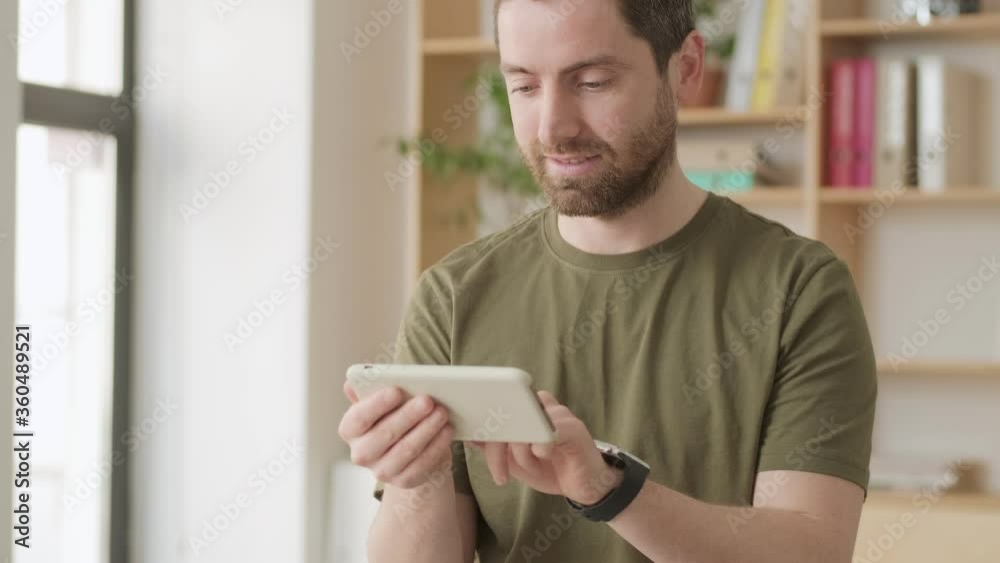 A handsome positive man is using his smartphone standing in the office A handsome positive man is using his smartphone standing in the office