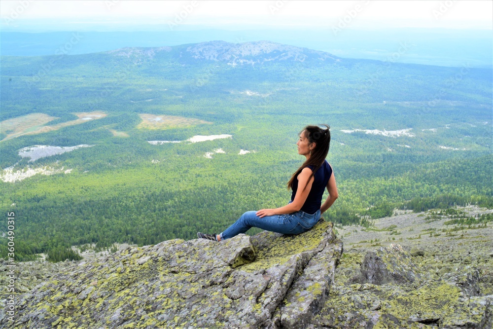 A girl sits on a high mountain and looks into the distance