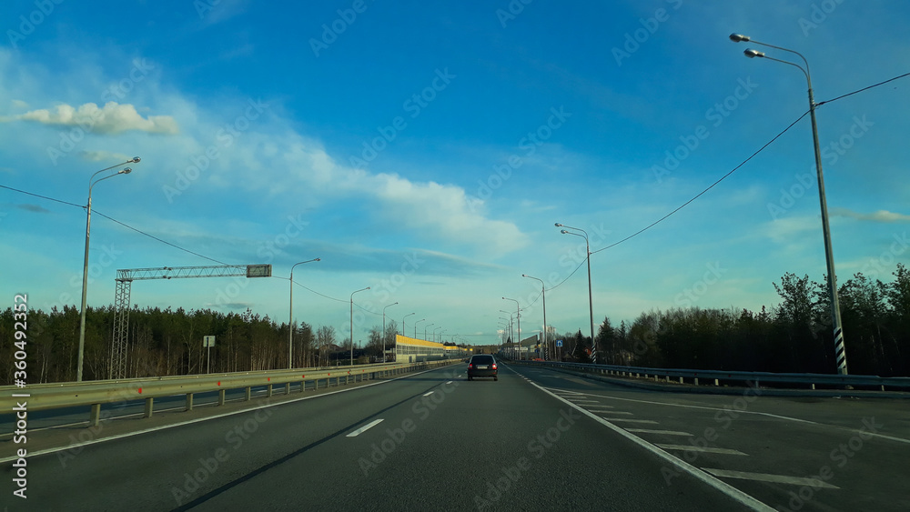 A road or highway leading to the horizon. View from the car window. Northern dim summer, blue sky with white clouds. Journey, the way home.