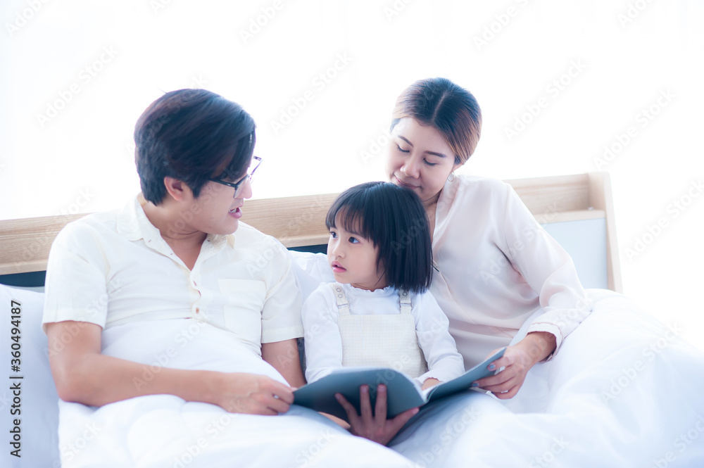Asian parents are telling stories to their daughters before bed. The daughter listened excitedly and surprised her face. On the bed under a white quilt Asian parents are telling stories to their daughters before bed. The daughter listened excitedly and surprised her face. On the bed under a white quilt