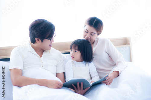 Asian parents are telling stories to their daughters before bed. The daughter listened excitedly and surprised her face. On the bed under a white quilt