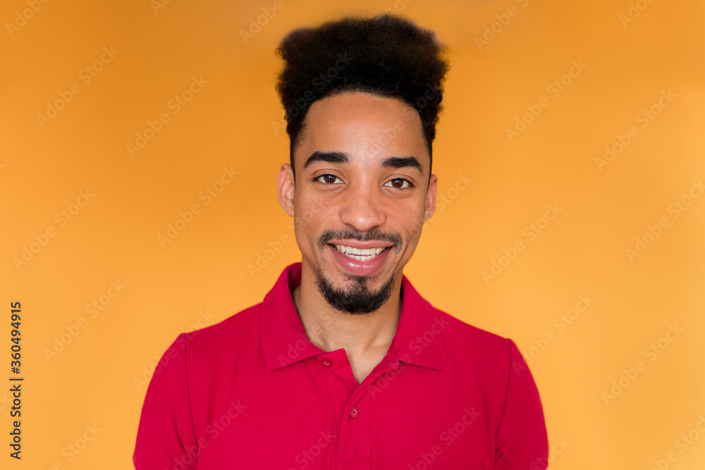 Close up inside portrait of arrican american man in red t-shirt looking at camera and smiling isolated over yellow background