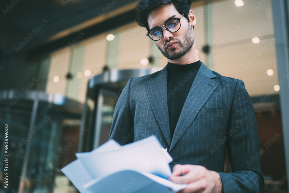 Pensive confident executive manager looking attentively at accounting reports and checking information standing outdoors.Successful entrepreneur reading financial paper documentation on street Pensive confident executive manager looking attentively at accounting reports and checking information standing outdoors.Successful entrepreneur reading financial paper documentation on street