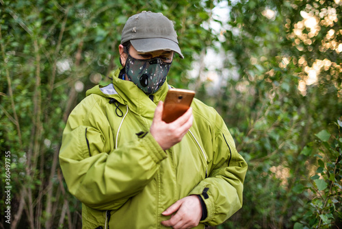 A girl wearing respirator mask and dialing a smartphone walking in the forest at COVID-19 period.