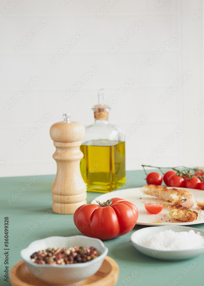 tomato wooden pepper mill and olive oil bottle on a green table