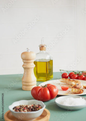 tomato wooden pepper mill and olive oil bottle on a green table