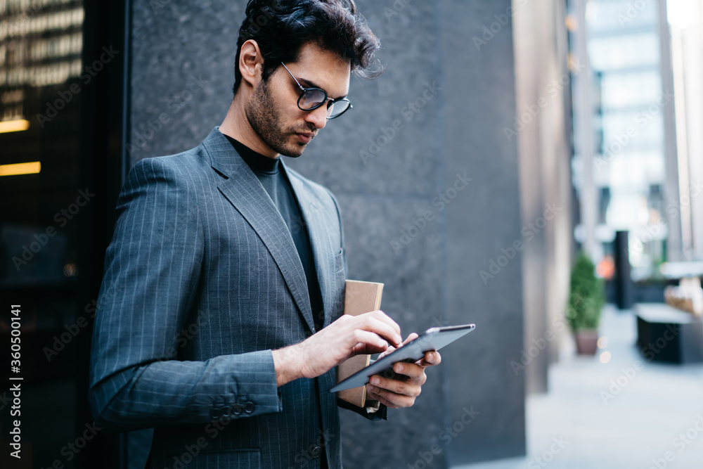 Pensive proud CEO in formal wear updating application with financial news on digital tablt connected to 4G internet on street.Confident businessman checking mail on touch pad near office building Pensive proud CEO in formal wear updating application with financial news on digital tablt connected to 4G internet on street.Confident businessman checking mail on touch pad near office building