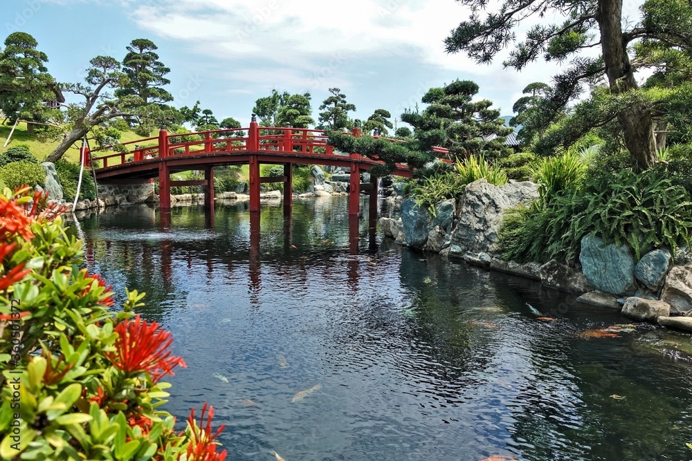Japanese style park. Sunny summer day, colorful fish swim in the river. The shores are connected by a bright red arched bridge. Around the picturesque trees. Vietnam. Japanese style park. Sunny summer day, colorful fish swim in the river. The shores are connected by a bright red arched bridge. Around the picturesque trees. Vietnam.