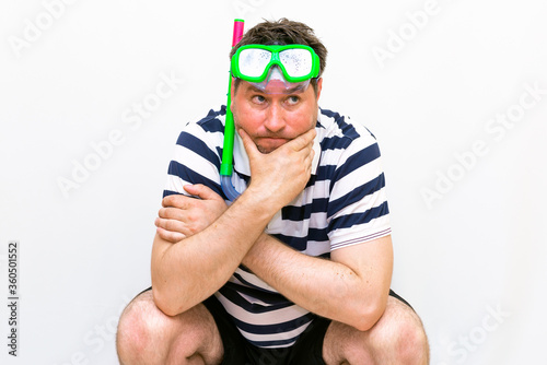 Front view close up squat thinking Man with snorkeling mask for diving stands on white wall