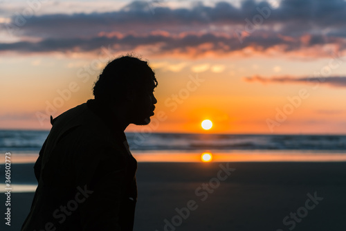 A silhouette of black male man with dreadlocks on a sunny beach with a sunset. Thinking and clarity in the great outdoors. Walking and fresh air for good positive mental health