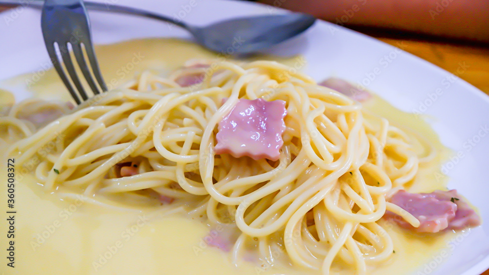The spaghetti carbonara with fried cheese in a white plate on the table. The spaghetti carbonara with fried cheese in a white plate on the table.