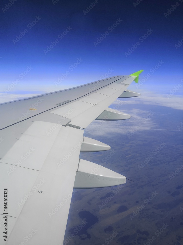 Wing of a flying plane against the background of blue sky and clouds