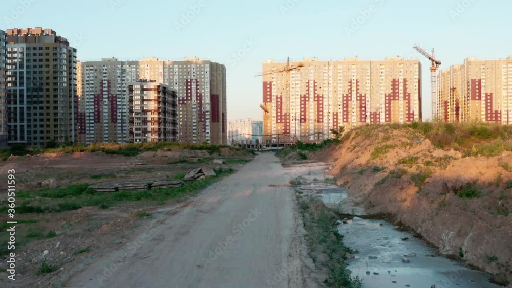 Aerial view. A dirt road near a construction site on the outskirts of the city on a summer evening at sunset. Construction of residential apartments in the city Aerial view. A dirt road near a construction site on the outskirts of the city on a summer evening at sunset. Construction of residential apartments in the city