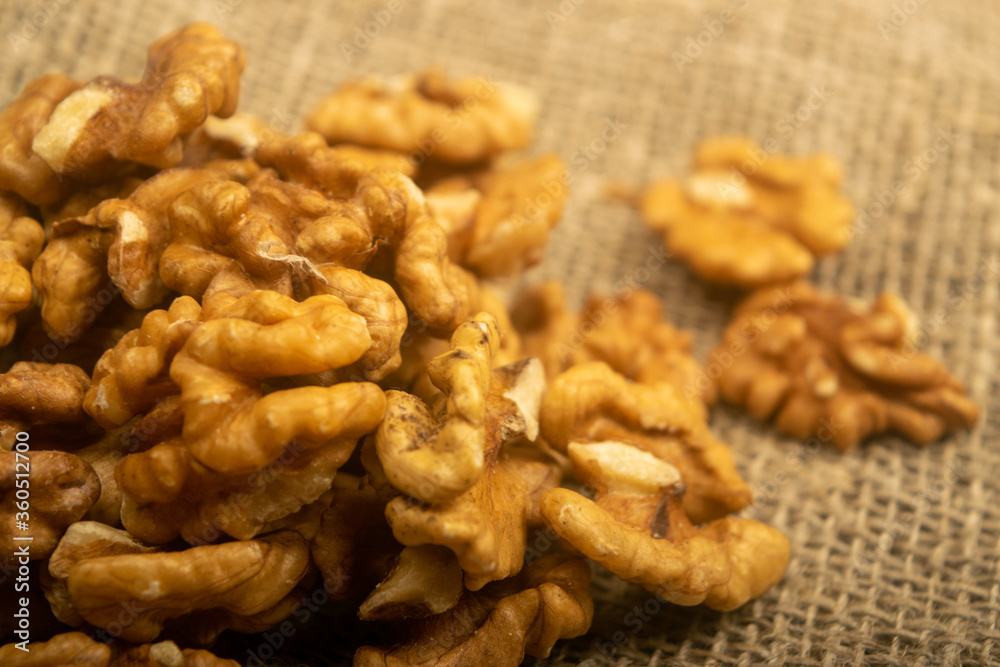 Peeled walnuts in bulk on a wooden table covered with rough-textured burlap. Healthy diet. Fitness diet. Close up. Peeled walnuts in bulk on a wooden table covered with rough-textured burlap. Healthy diet. Fitness diet. Close up.
