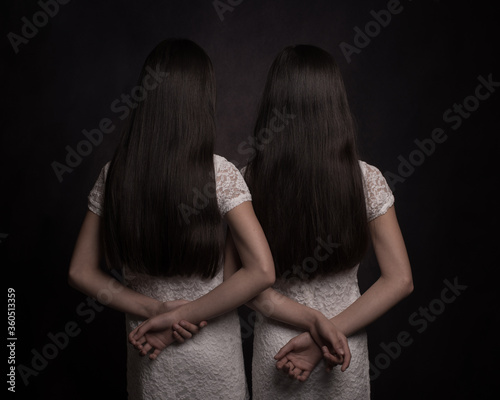 Twin sisters with black long hair and white dress with arms and hands resting on back seen from behind in dark painterly studio style