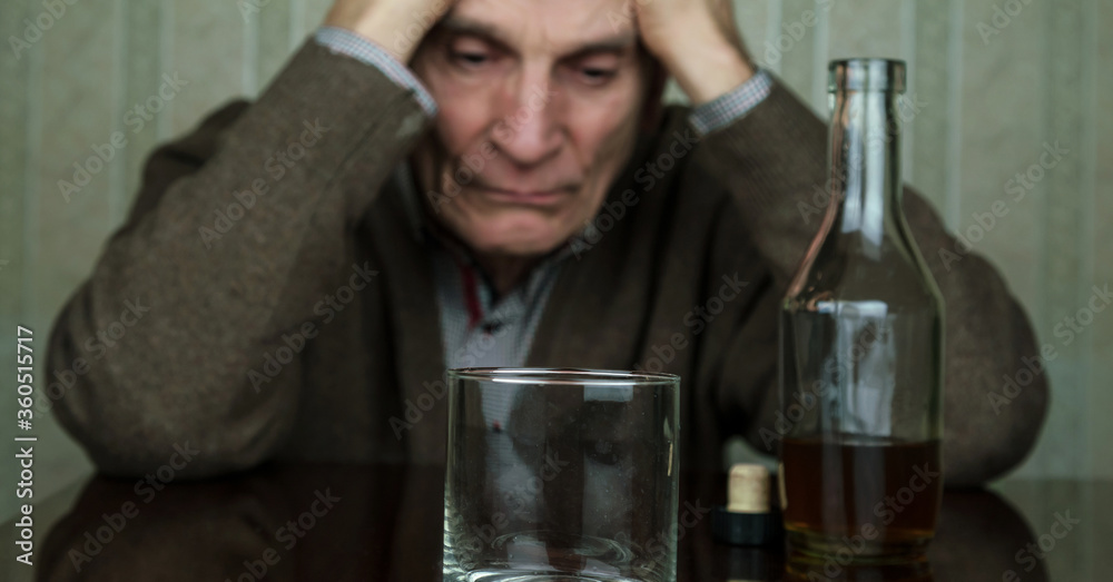 sad senior man sits near bottle with whiskey and empty glass holding hands on head sad senior man sits near bottle with whiskey and empty glass holding hands on head