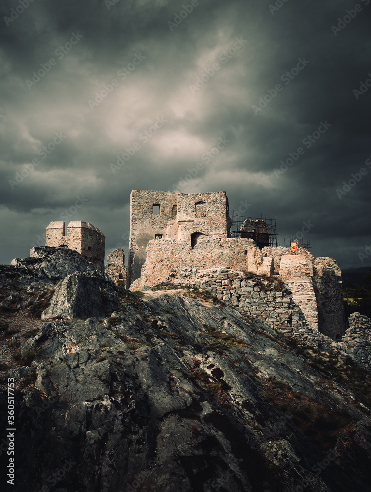 Dark and moody view of Hrusov Castle in Europe (Slovakia) before the storm. Old Ruins of castle on the dark rocks with rainbow on background.  Dramatic shot of castle on the hill with misty sky.