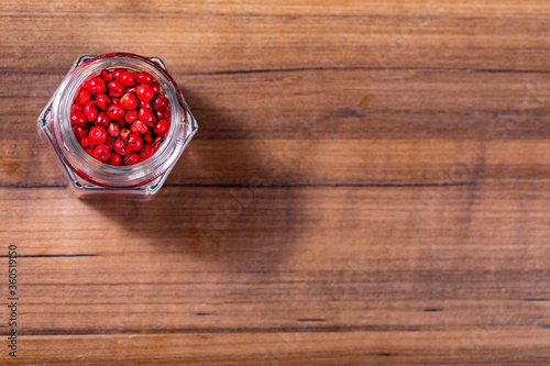 Closeup in glass jar with grains of red pepper on wooden background