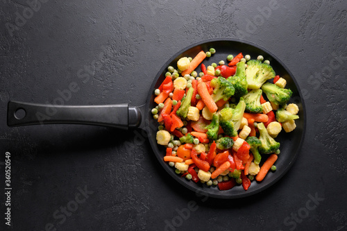 Frozen vegetables in frying pan on black background. View from above.