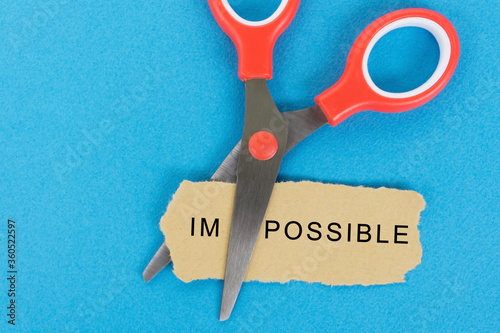 Scissor cutting the word 'impossible' in a piece of paper.