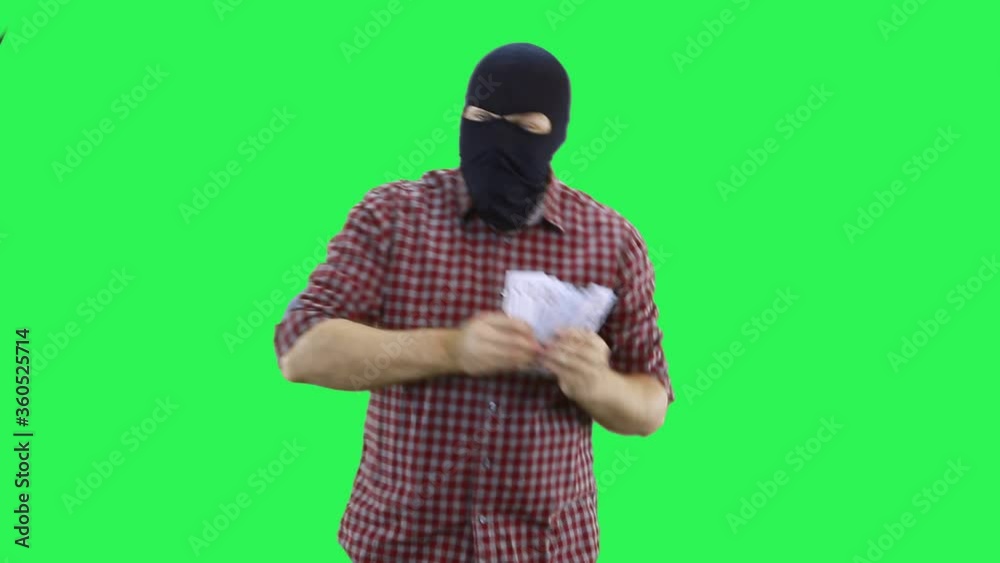 A man in a balaclava in a plaid shirt holds money in his hands and dances to rejoice at it. A man in a balaclava in a plaid shirt holds money in his hands and dances to rejoice at it.