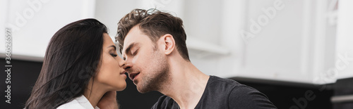 Panoramic crop of handsome man kissing attractive woman at home