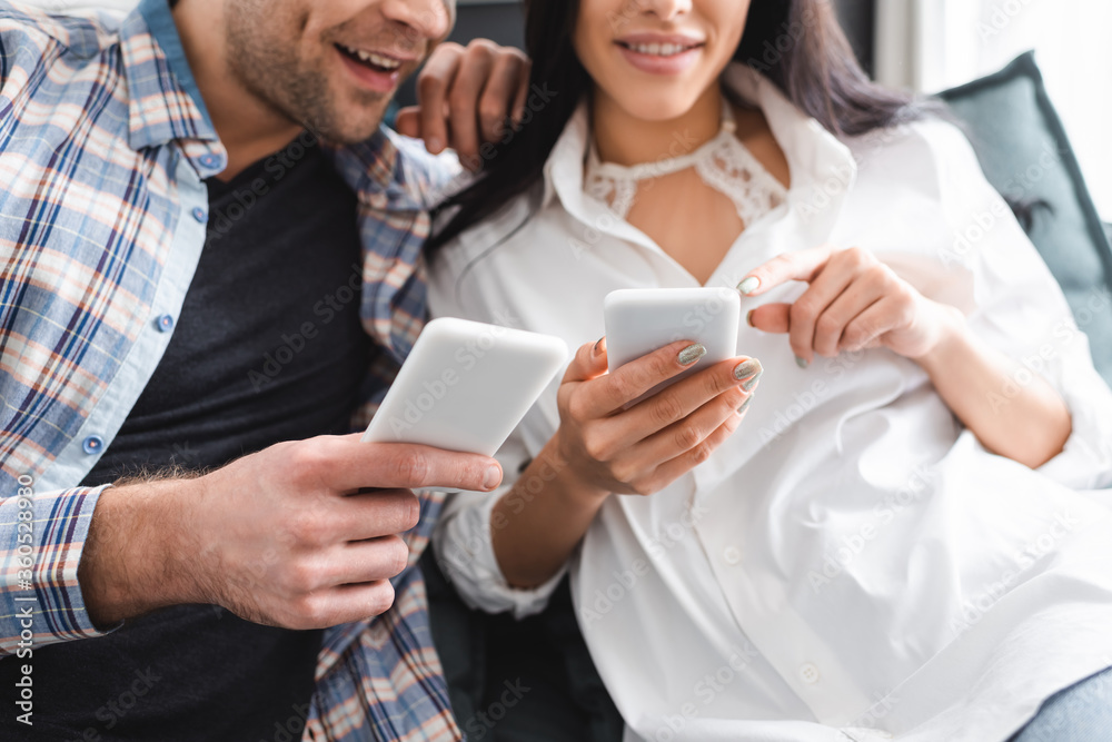 Cropped view of smiling woman pointing with finger at smartphone near boyfriend Cropped view of smiling woman pointing with finger at smartphone near boyfriend