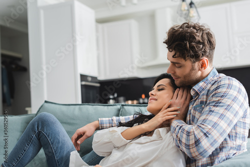 Handsome man hugging and touching hair of beautiful smiling girlfriend on sofa © LIGHTFIELD STUDIOS