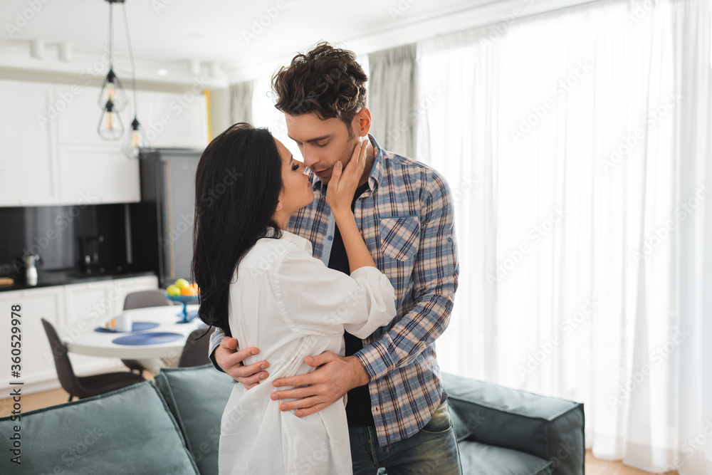 Beautiful woman kissing and hugging boyfriend in living room Beautiful woman kissing and hugging boyfriend in living room