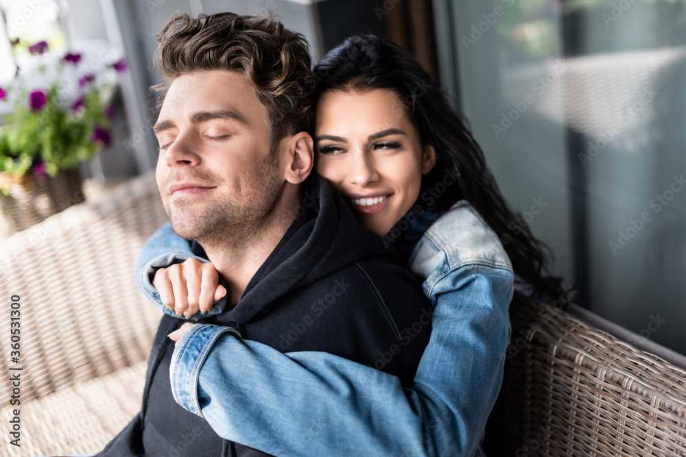 Fototapeta premium Beautiful smiling girl hugging handsome boyfriend on wicker sofa on terrace