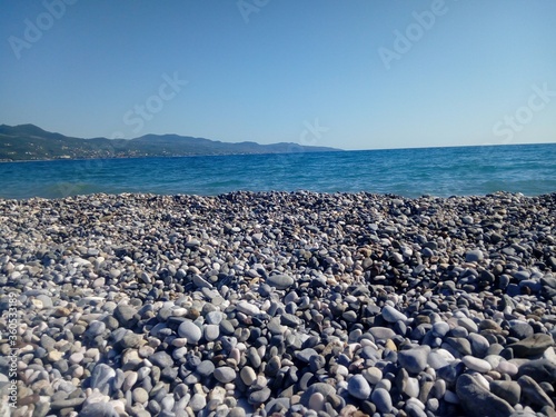 View of a blue sea filled with stones with a tall mountain and a blue sky in the background photo