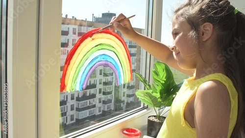 Girl painting rainbow on window during quarantine at home. Thank You Essential Workers message concept.