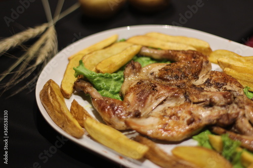 Chicken tabaka with fried potatoes and greens on a color background.
