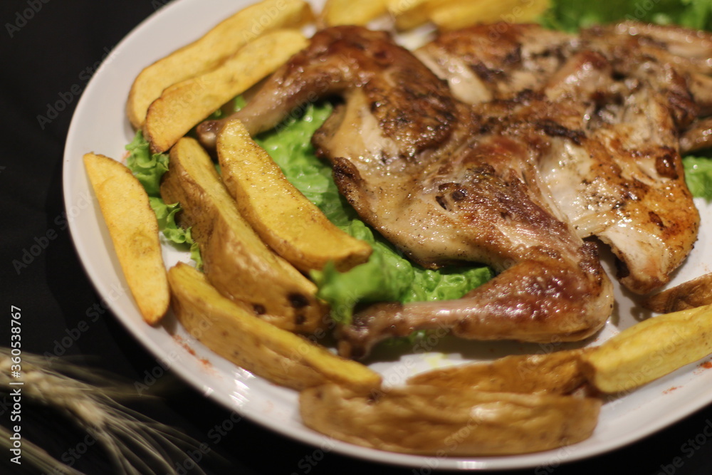 Chicken tabaka with fried potatoes and greens on a color background. Chicken tabaka with fried potatoes and greens on a color background.